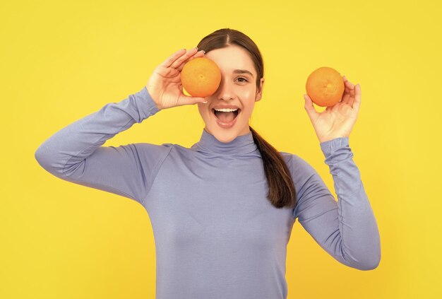 Mulher jovem espantada segurando frutas cítricas laranja na saúde de fundo amarelo