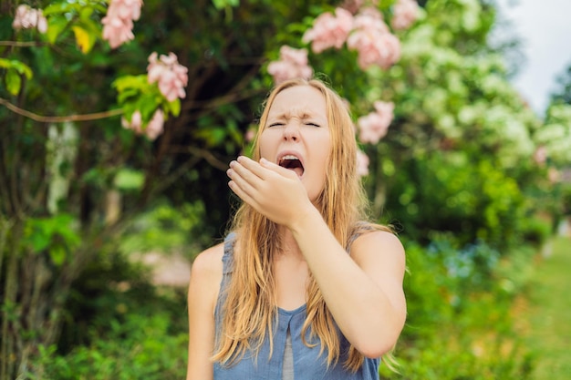 Mulher jovem espirra no parque no contexto de uma árvore em flor. conceito de alergia ao pólen