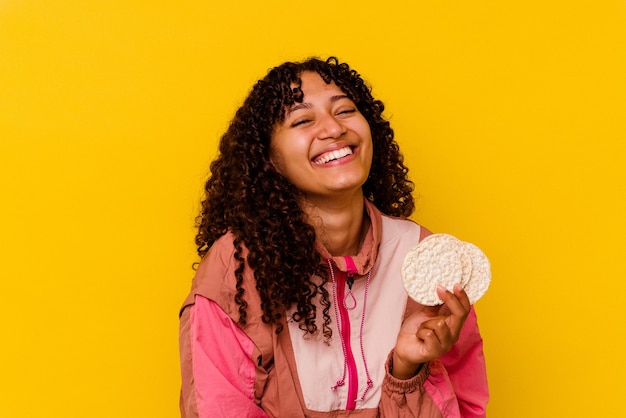 Foto mulher jovem esporte de raça mista segurando um bolo de arroz isolado no fundo amarelo, rindo e se divertindo.