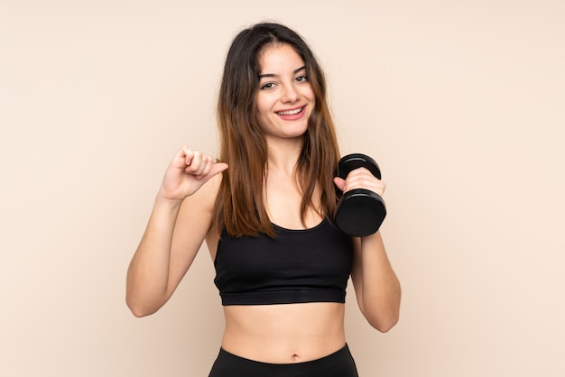 Mulher jovem esporte fazendo halterofilismo bege orgulhoso e satisfeito