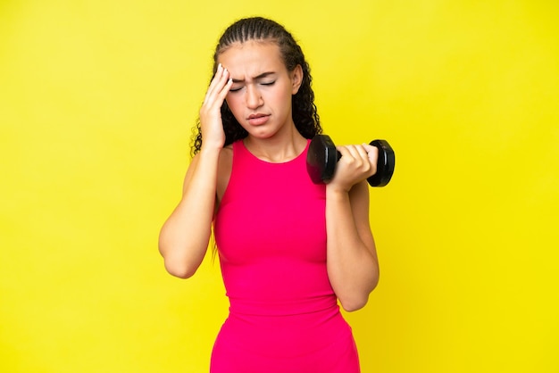 Mulher jovem esporte fazendo levantamento de peso isolado em fundo amarelo com dor de cabeça