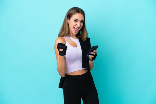 Mulher jovem esporte isolada em um fundo azul com o telefone em posição de vitória