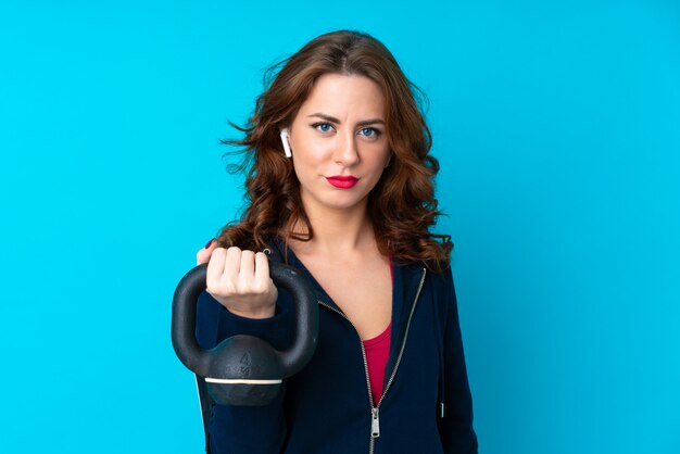 Mulher jovem esporte isolado azul fazendo levantamento de peso com kettlebell e olhando para a frente