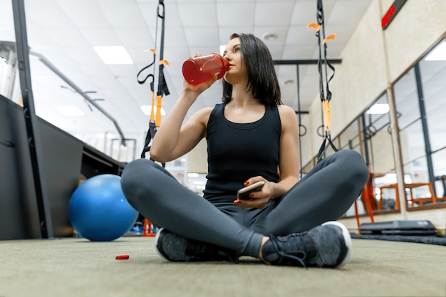 Mulher jovem esportes descansando no chão após exercícios no ginásio, água potável