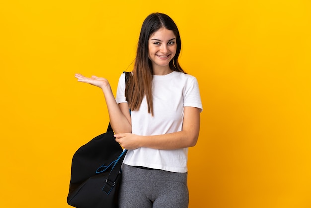 Mulher jovem esportiva com bolsa esportiva isolada em amarelo segurando o imaginário de copyspace na palma da mão para inserir um anúncio