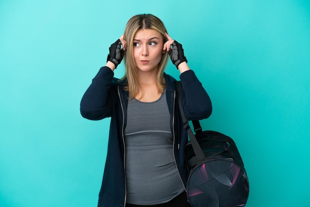 Mulher jovem esportiva com bolsa esportiva isolada em fundo azul, tendo dúvidas e pensando