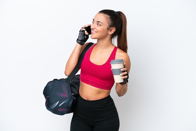 Mulher jovem esportiva com bolsa esportiva isolada em fundo branco segurando café para levar e um celular