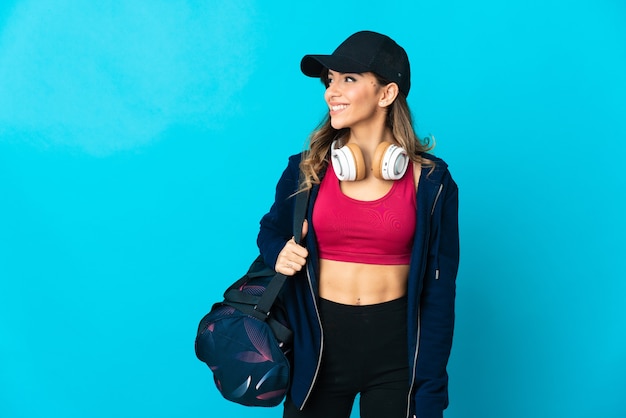 Foto mulher jovem esportiva com bolsa esportiva isolada na parede azul, olhando para o lado e sorrindo