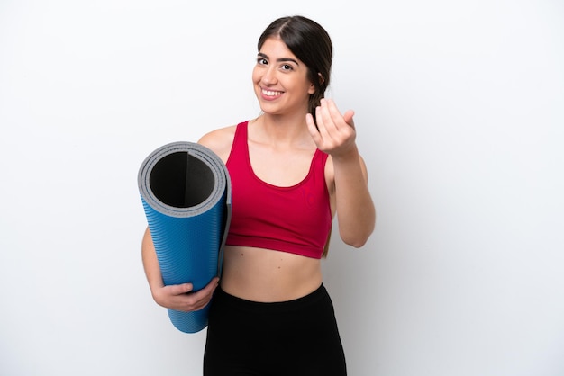 Mulher jovem esportiva indo para aulas de ioga enquanto segura um tapete isolado no fundo branco, convidando para vir com a mão Feliz por você ter vindo