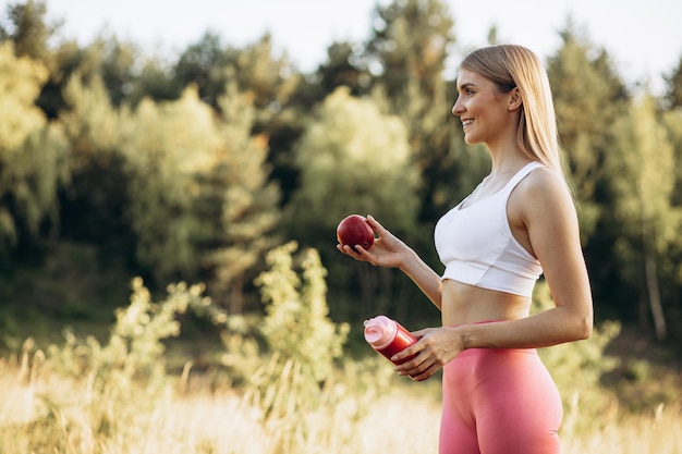 Mulher jovem esportiva no parque comendo maçã e água potável