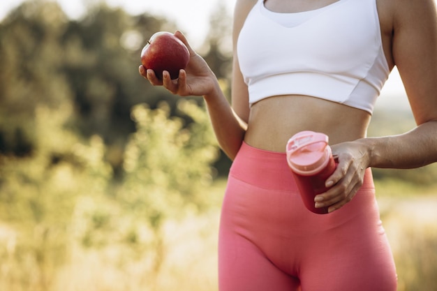 Mulher jovem esportiva no parque comendo maçã e água potável