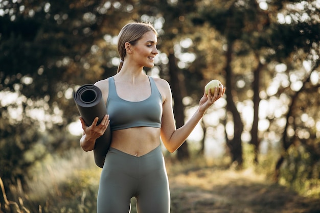 Mulher jovem esportiva no parque segurando tapete e maçã