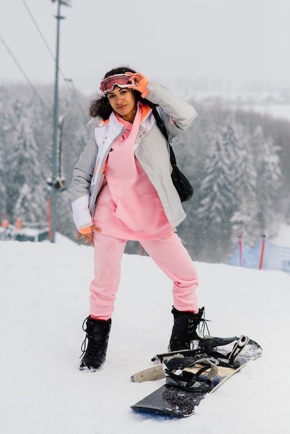 Mulher jovem esquiadora afro-americana com snowboard sorrindo e levantando o polegar