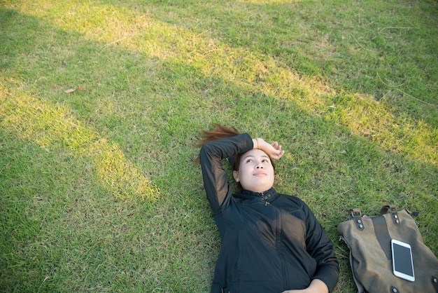 Mulher jovem está descansando em uma grama que tem bolsa e telefone