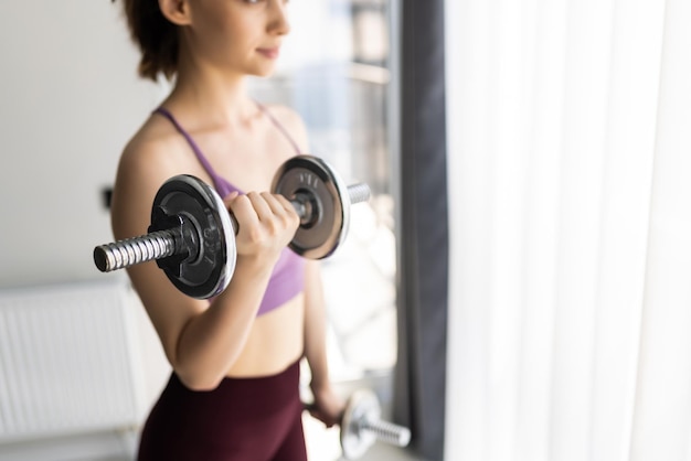 Mulher jovem está se exercitando com halteres em casa.