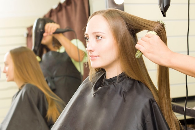 Mulher jovem está secando o cabelo com um secador de cabelo.