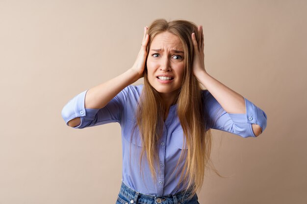 Mulher jovem estressada e confusa, segurando a cabeça contra um fundo bege