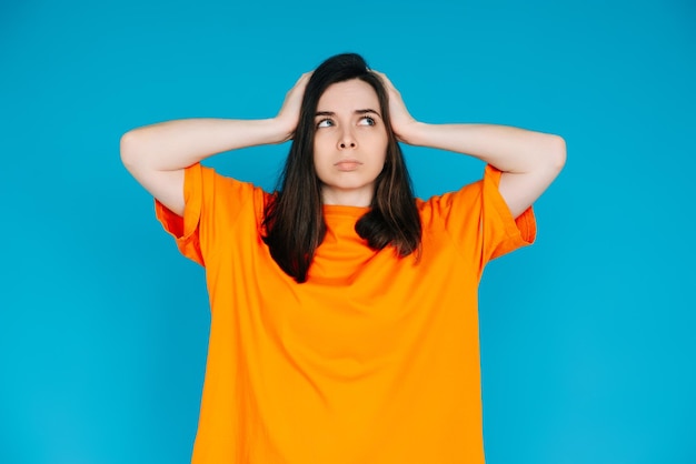 Mulher jovem estressada expressando descontentamento tocando a cabeça emoções negativas frustração isolada fundo azul