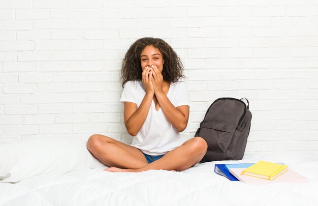 Mulher jovem estudante afro-americano na cama rindo de algo, cobrindo a boca com as mãos.