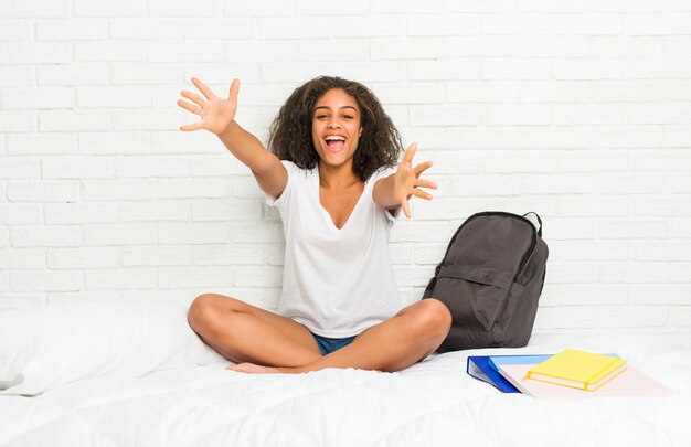 Mulher jovem estudante afro-americano na cama se sente confiante dando um abraço para a câmera.
