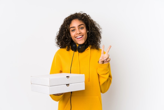 Mulher jovem estudante afro-americano segurando pizzas alegres e despreocupadas, mostrando um símbolo de paz com os dedos.