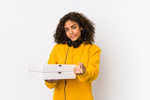 Mulher jovem estudante afro-americano segurando pizzas apontando com o dedo para você como se estivesse convidando se aproximar.