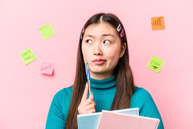 Mulher jovem estudante asiática segurando livros isolados em fundo rosa