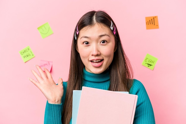 Mulher jovem estudante asiática segurando livros isolados em fundo rosa