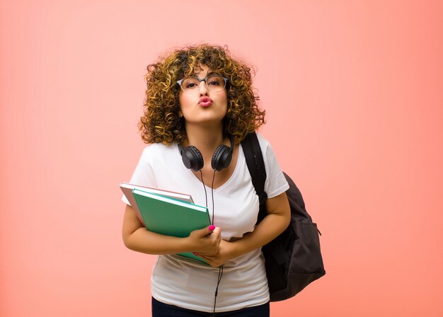 Mulher jovem estudante bonita pressionando os lábios com uma expressão fofa, divertida, feliz e adorável, mandando um beijo contra a parede rosa