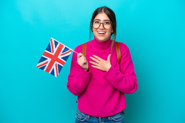 Mulher jovem estudante caucasiana segurando a bandeira inglesa isolada em fundo azul surpresa e chocada ao olhar para a direita