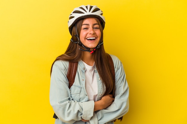 Mulher jovem estudante caucasiana usando um capacete de bicicleta isolado em fundo amarelo, rindo e se divertindo.