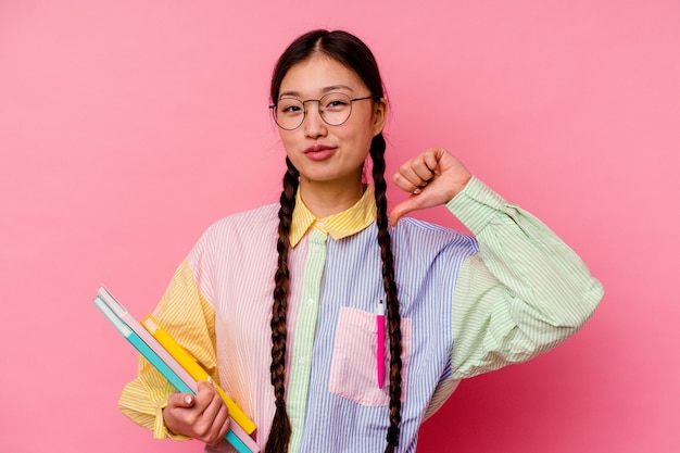 Mulher jovem estudante chinesa segurando livros vestindo uma camisa multicor da moda e uma trança, isolada no fundo rosa, sente-se orgulhosa e autoconfiante, exemplo a seguir.