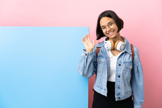 Mulher jovem estudante de raça mista com um grande banner sobre fundo isolado saudando com a mão com expressão feliz