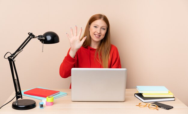 Mulher jovem estudante em um local de trabalho com um laptop, contando cinco com os dedos