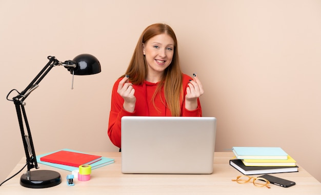 Mulher jovem estudante em um local de trabalho com um laptop fazendo gesto de dinheiro