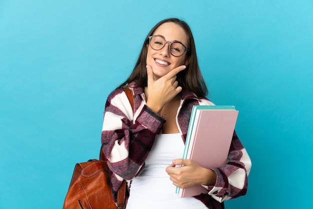 Mulher jovem estudante feliz e sorridente em uma parede isolada