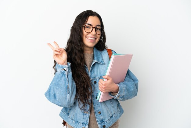 Foto mulher jovem estudante isolada em um fundo branco sorrindo e mostrando sinal de vitória