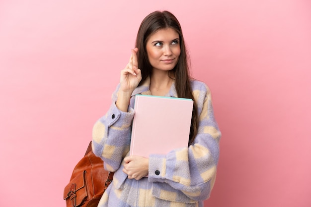 Mulher jovem estudante isolada em um fundo rosa com os dedos se cruzando e desejando o melhor