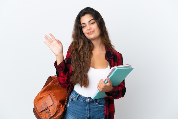 Mulher jovem estudante isolada no fundo branco saudando com a mão com expressão feliz