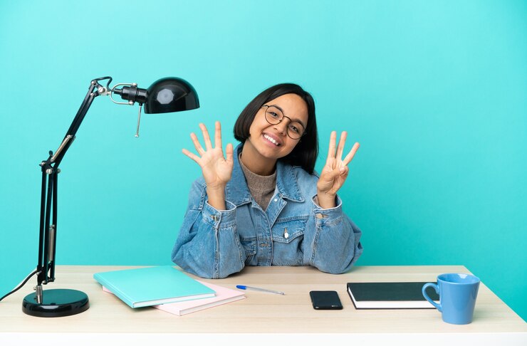 Foto mulher jovem estudante mestiça estudando em uma mesa contando oito com os dedos