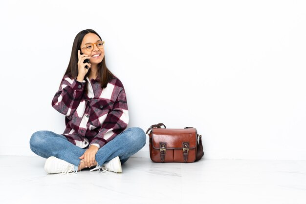 Mulher jovem estudante sentada no chão, conversando com o telefone celular