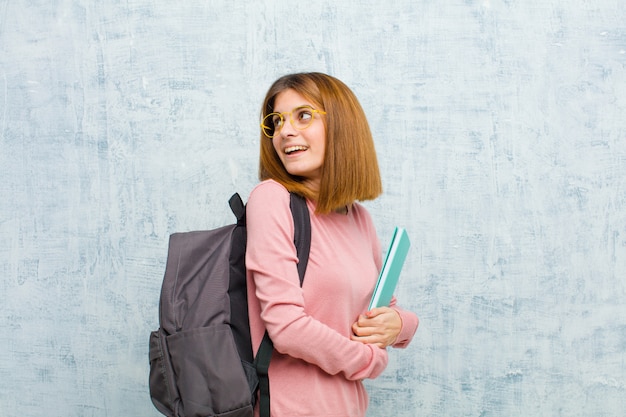 Mulher jovem estudante sorrindo alegremente se sentindo feliz satisfeito e relaxado com os braços cruzados e olhando para o lado