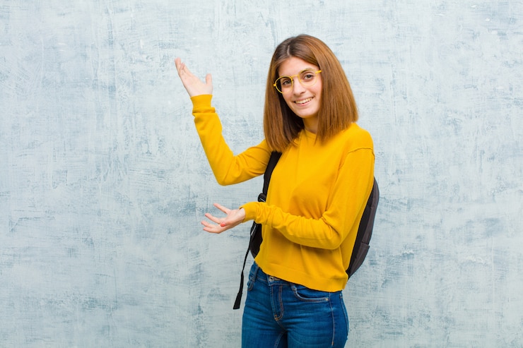 Foto mulher jovem estudante sorrindo com orgulho e confiança, sentindo-se feliz e satisfeito e mostrando um conceito no espaço da cópia contra a parede da parede do grunge