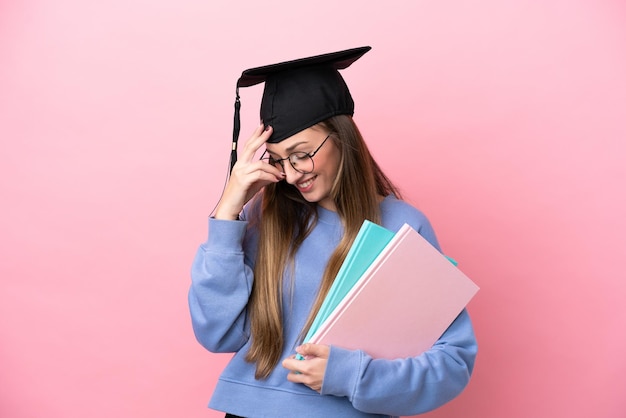 Mulher jovem estudante usando um chapéu de pós-graduação isolado no fundo rosa rindo