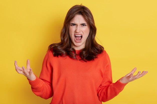 Foto mulher jovem europeia emocional com raiva gritando sobre o rosto amarelo, carrancudo, levantando as mãos, usando fechamento casual, expressando emoções negativas.