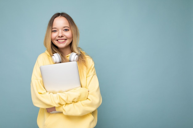 Mulher jovem europeia feliz e sorridente estudante usando um capuz amarelo segurando o caderno sobre azul isolado