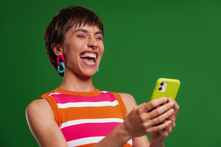 Foto mulher jovem excitada segurando um smartphone e sorrindo enquanto está de pé contra o fundo verde