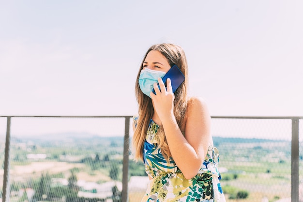 Mulher jovem falando ao telefone com uma máscara médica