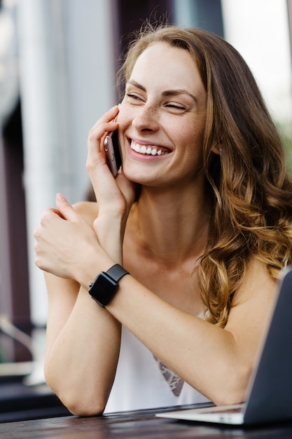 Mulher jovem falando ao telefone no café e usando o laptop