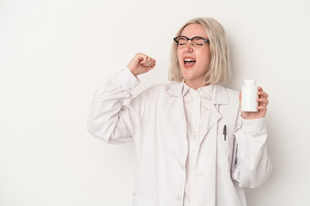 Mulher jovem farmacêutico segurando comprimidos isolados no fundo branco, levantando o punho após uma vitória, o conceito de vencedor.